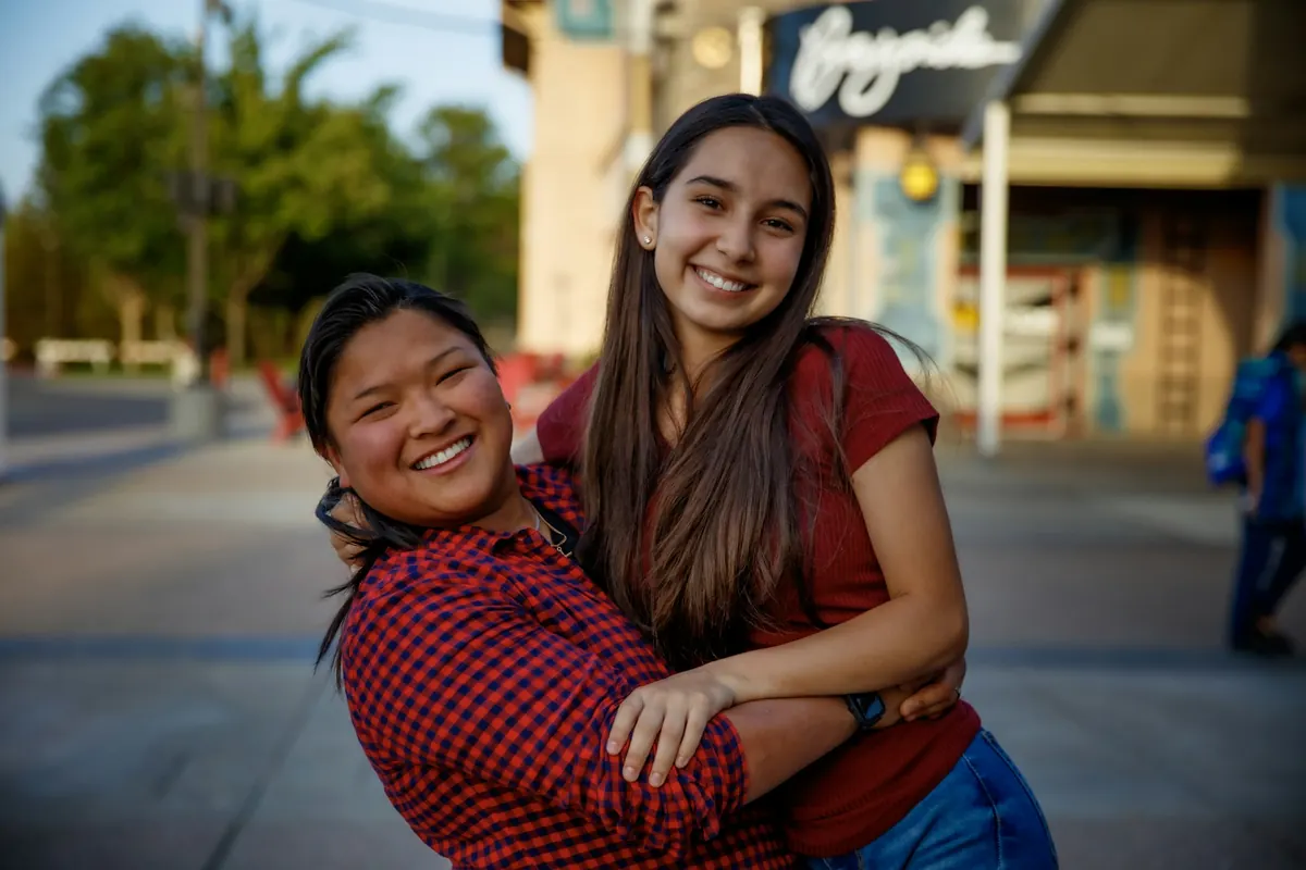 Una mamá abraza a su hija adolescente en la calle; las dos sonríen