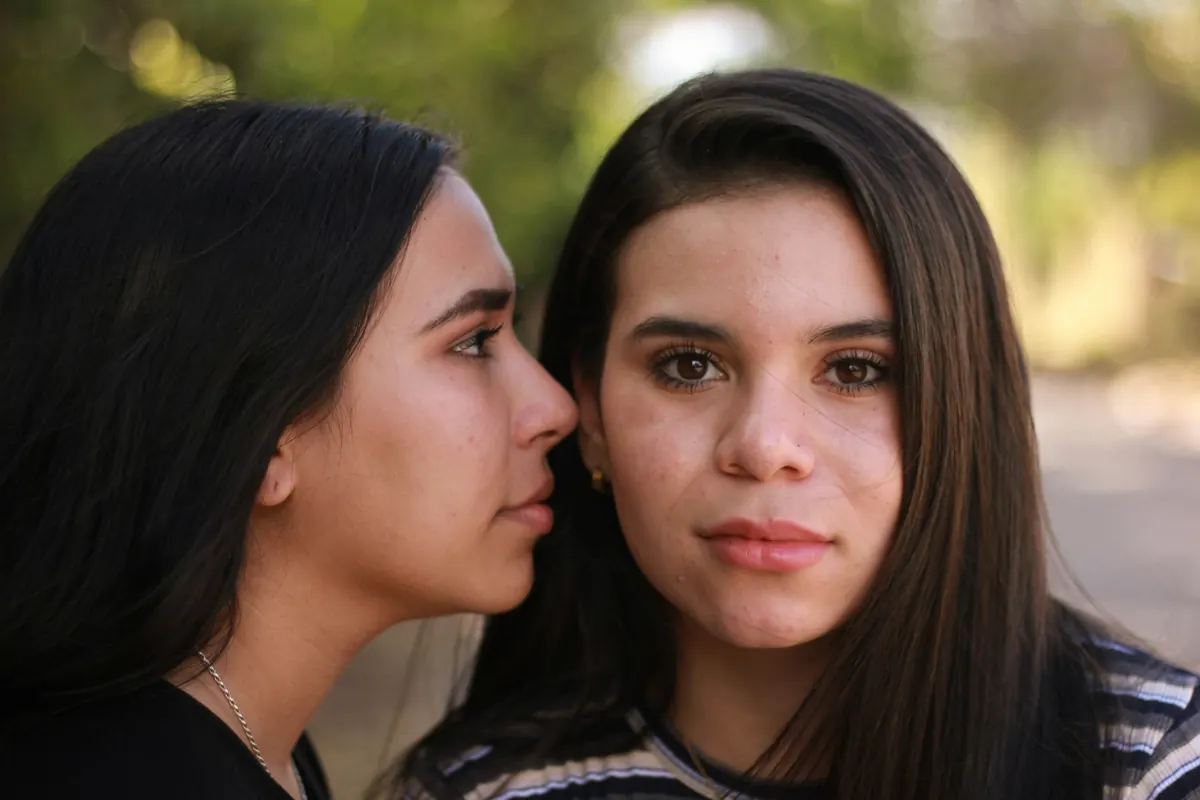 Dos jóvenes muy cerca, una apoyada en la otra, mirando a la cámara