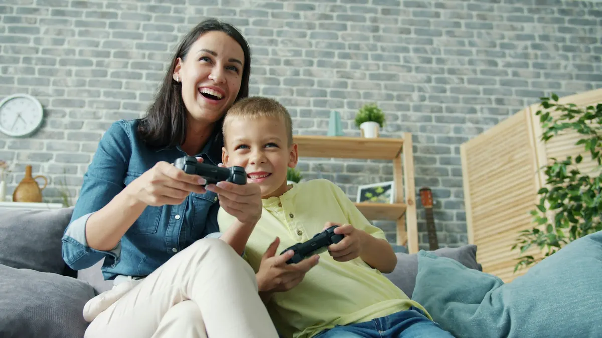 Una mamá y su hijo juegan videojuegos en el sillón y se ríen